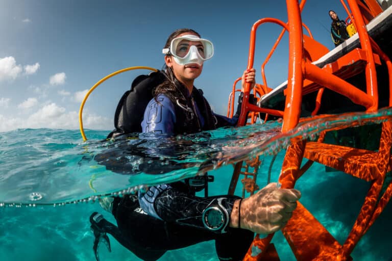 Happy scuba diver smiling as she exits the water onto a boat in the ocean during a referral dive in Cancun.
